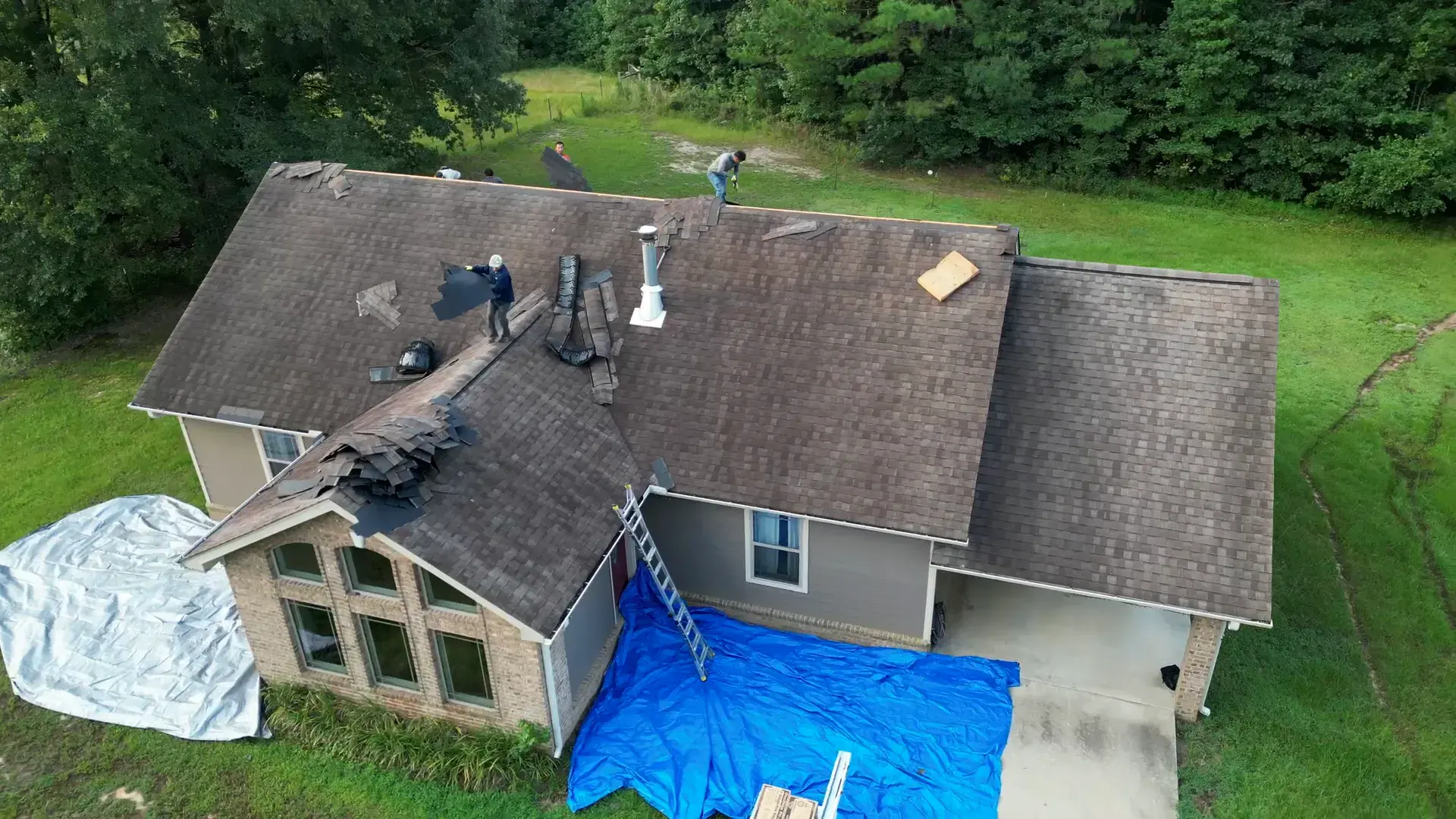 The same brick ranch before the job, with aging windows below a worn roof mid tear-off